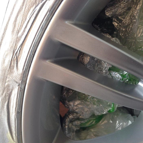 Close up of car alloy wheel scuff damage during repair preparation with masked tyre and surface ready for refinishing process